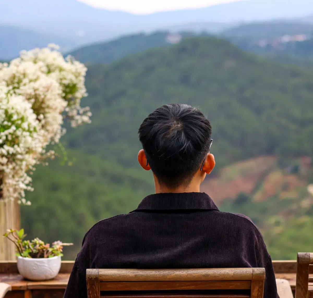 Homme de dos sur une terrasse fleurie face aux montagnes