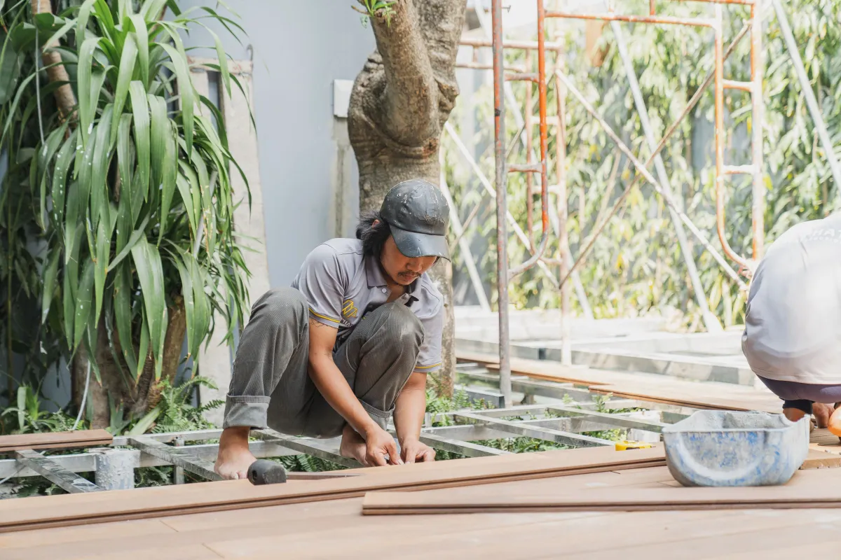 Artisan à genoux posant des lames de terrasse, outils au premier plan