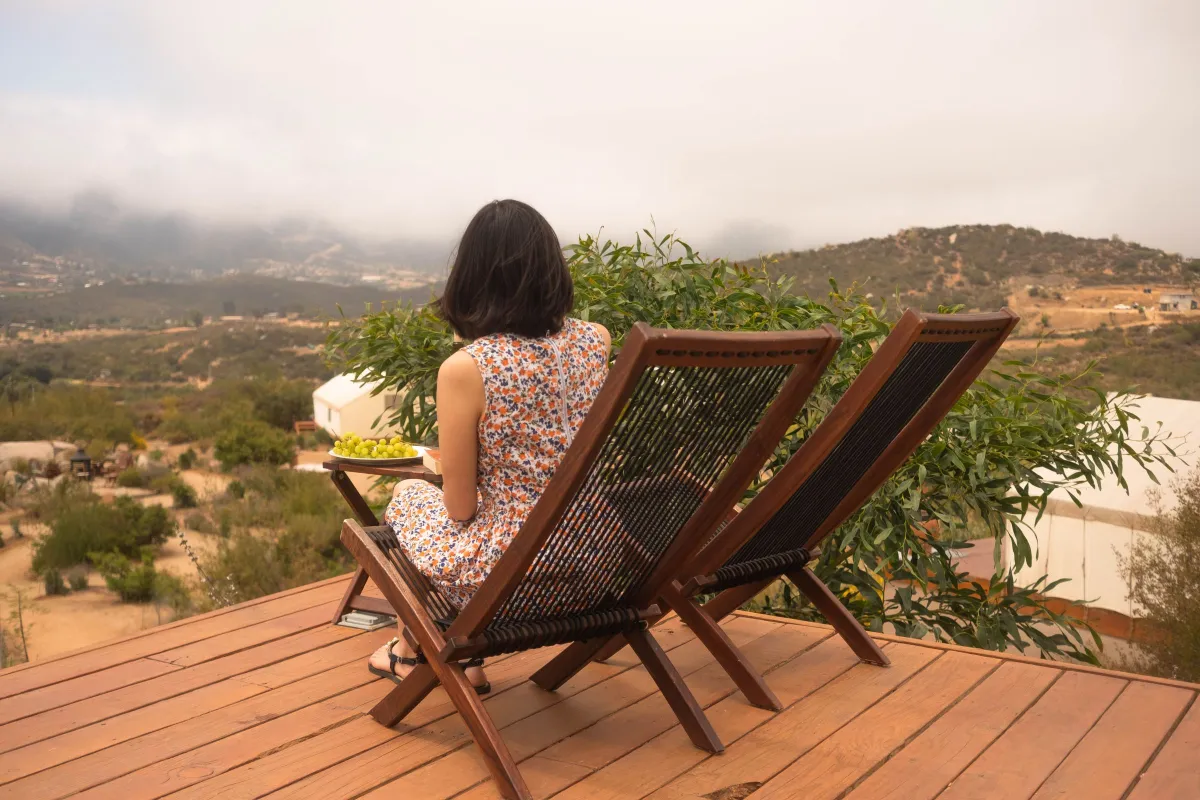 Femme assise sur une terrasse en bois face aux collines